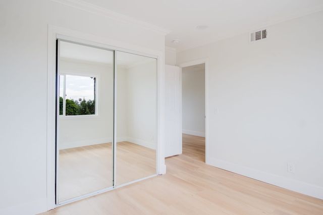 Empty freshly painted bedroom with light wood floors, mirrored sliding closet doors and an open doorway to the hall