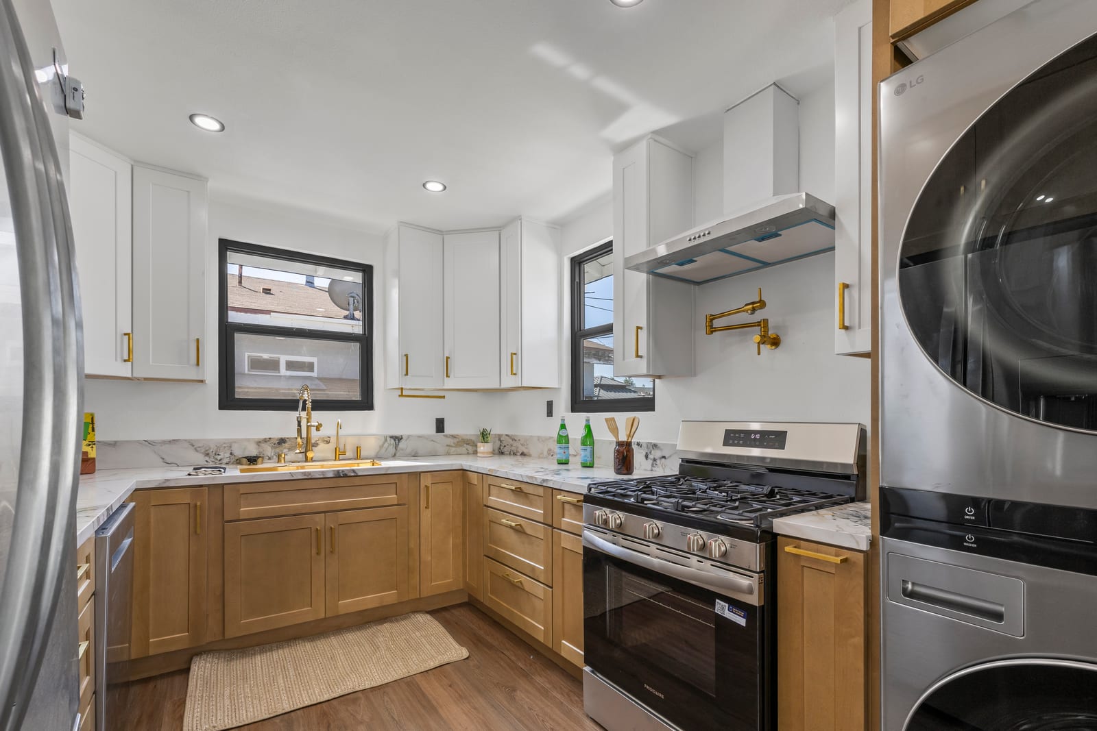 A renovated U-shaped kitchen with white upper cabinets, wood lower cabinets, gold hardware, marble-look counters, a gas range and a stacked washer and dryer.