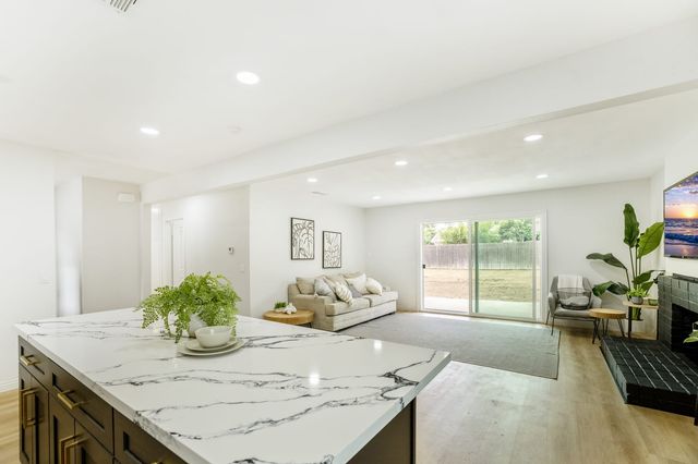 An open living area seen from a marble-look kitchen island, with a sofa, a fireplace painted black and a sliding glass door to the backyard.