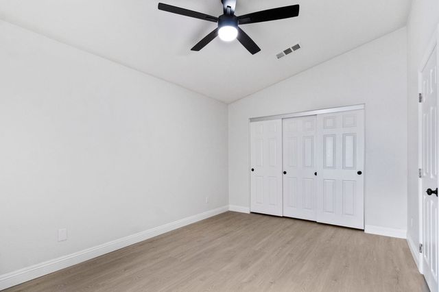 An empty bedroom in a Victorville house with a vaulted ceiling, a black ceiling fan, wood-look floors and white sliding closet doors.