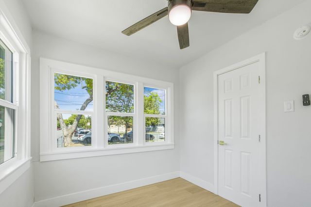 An empty front room in an Ontario house with a ceiling fan, light wood floors and a row of white-framed windows looking out to a tree-lined street.