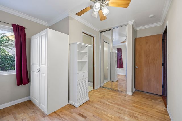 A Rancho Cucamonga bedroom with wood floors, a white wardrobe and shelf unit, mirrored closet doors and an open door to a bathroom