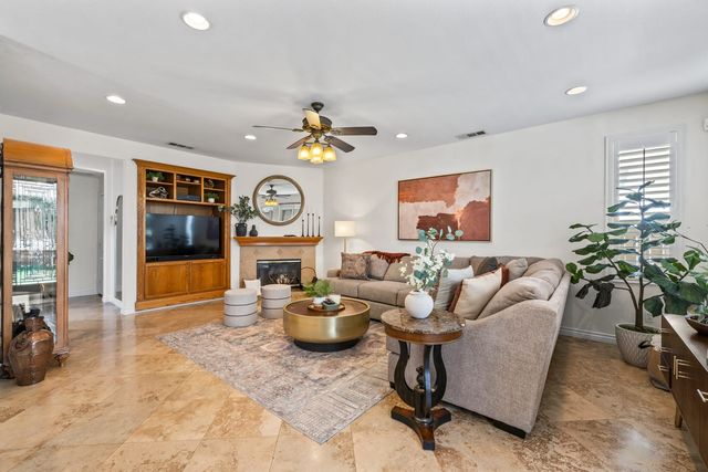 A staged Corona living room with a sectional sofa, a round brass coffee table, a corner fireplace and a built-in wood media cabinet on tile floors