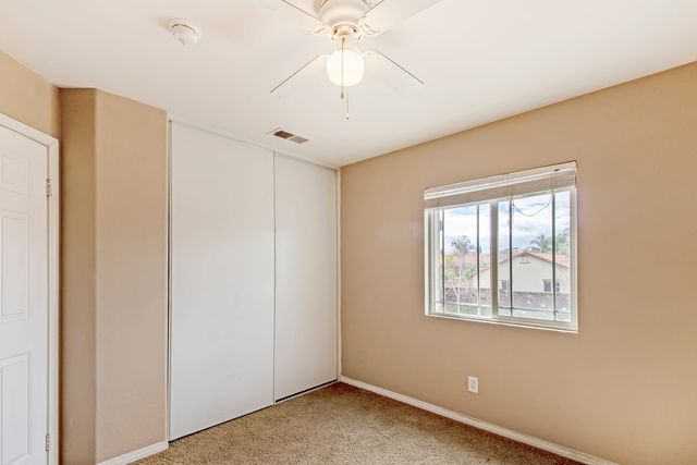 An empty Menifee bedroom with tan walls, carpet, a white sliding closet and a window looking out to neighboring tile roofs