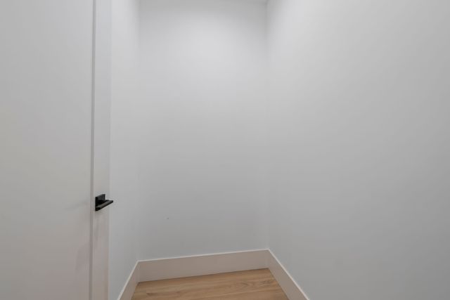 Small empty room with white walls, an open white door with a black lever handle and light wood flooring