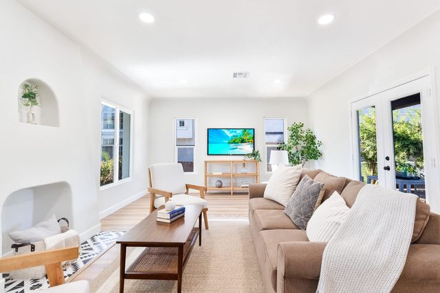Living room with an arched wall niche, a tan sofa beside a wood coffee table, a wall-mounted screen and French doors opening to a garden
