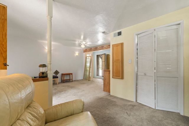 Older living area with carpet, a cream leather recliner, louvered closet doors, a wallpaper border and a doorway to a sunlit back room