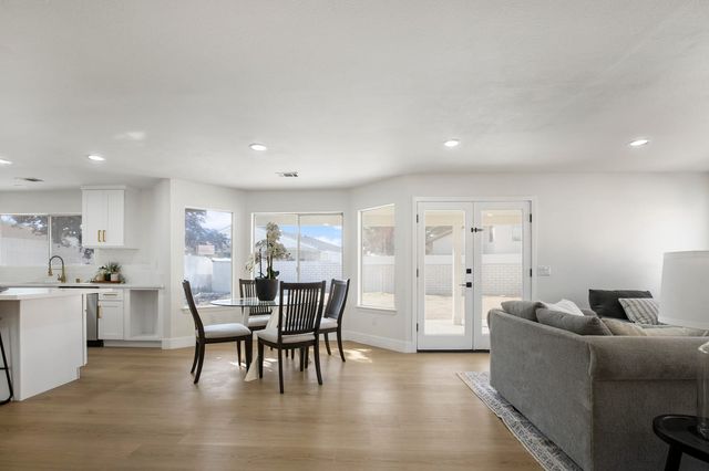 Open living and dining area with a round glass table and four dark wood chairs, a gray sofa, white kitchen cabinets and French doors to a covered patio