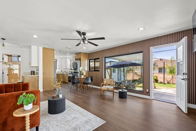 Open-plan living room with a rust velvet sofa, a slatted wood accent wall, a large picture window onto a covered patio and an open door to the yard