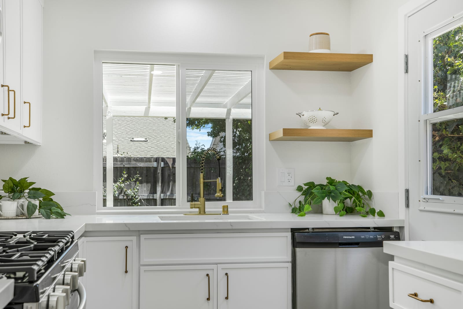 White kitchen with open wood shelving and a window to a covered patio