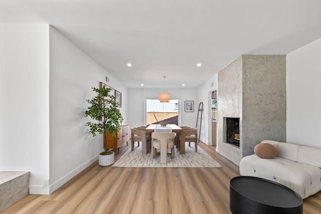 Staged Claremont dining area with an upholstered chair set around a wood table, a textured plaster fireplace, a potted tree and wood-look flooring