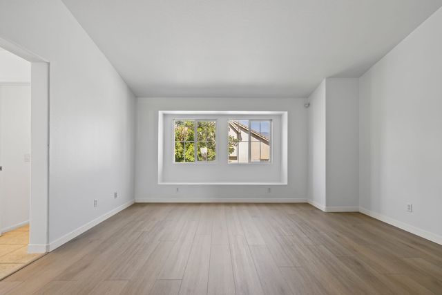Empty living room with light wood-look flooring, white walls, a vaulted ceiling and a pair of windows in a deep recessed alcove