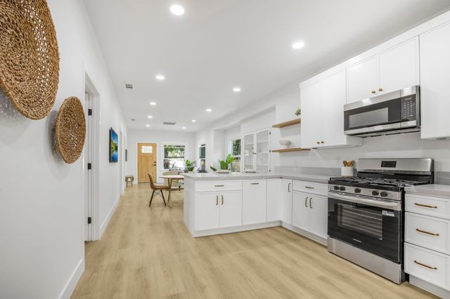 Renovated kitchen in a Long Beach house with white cabinets, a stainless range and microwave, light plank floors and a hallway leading to the front door.