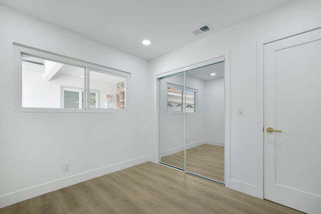 Vacant, freshly painted bedroom in a Santa Ana house with mirrored sliding closet doors, a wood-look floor, recessed lights and an interior window.