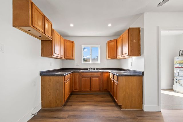 Empty kitchen with oak cabinets, dark laminate counters and a vinyl plank floor, no appliances, and a water heater visible through the next doorway