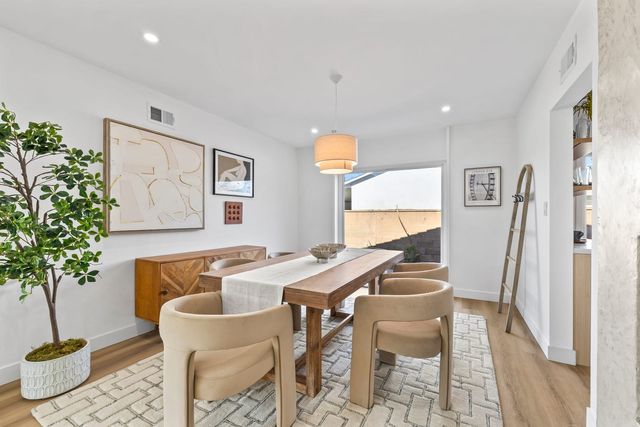 Staged dining room in a Claremont house with a long wood table, four upholstered chairs, a patterned rug, a wood sideboard and framed art, with a sliding door to a walled side yard